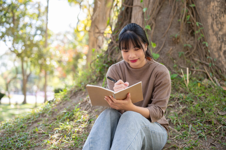 A young woman smiling as she writes in her notebook